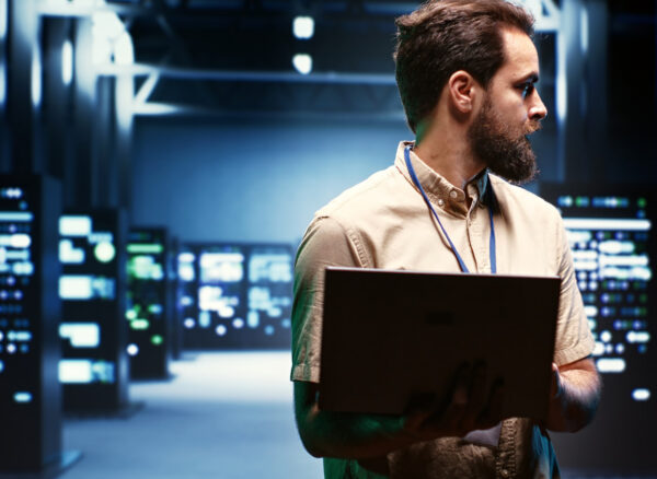 Supervisor using laptop to oversee energy consumption across server hub components and distributors. Serviceman ensuring high tech facility sensors for temperature and humidity are working properly